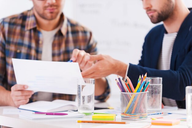 Trabajando juntos en un proyecto. Primer plano de dos hombres de negocios confiados en ropa casual elegante sentados juntos en la mesa y discutiendo algo