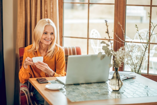 Trabajando. Mujer rubia de pelo largo sentada en la mesa y trabajando en una computadora portátil