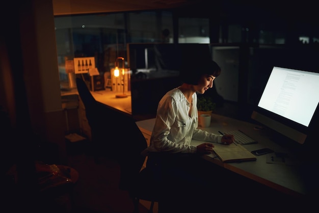 Foto trabajando en un plan tarde en la noche foto de una joven empresaria escribiendo en un cuaderno durante una noche en el trabajo