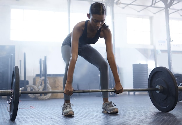 Trabajando en su fuerza central y estabilidad Captura de una joven deportista haciendo ejercicio con una barra en un gimnasio