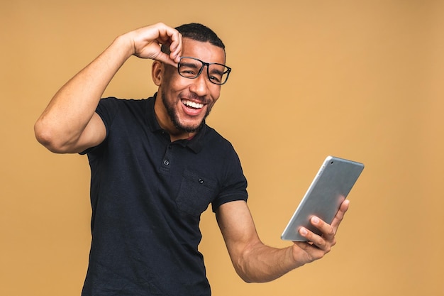 Trabajando en una tableta digital Retrato de un joven negro afroamericano feliz y sonriente sosteniendo una tableta digital mientras se encuentra aislado sobre un fondo beige