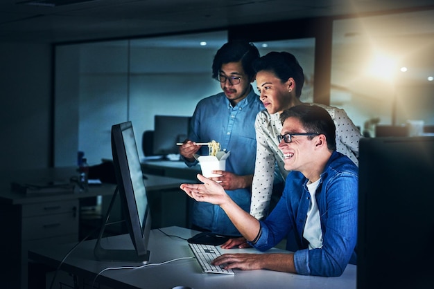 Trabajando el turno de noche Toma de un grupo de programadores trabajando juntos en una computadora en la oficina en el trabajo durante la noche