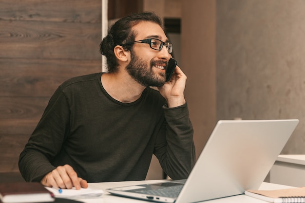 Trabajar desde casa. Un hombre en casa hablando por teléfono. Un, joven, sentado, en, un, computador portatil