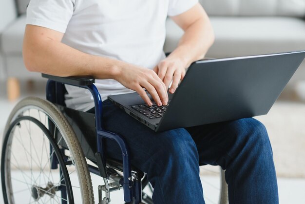 Trabajar en casa Persona masculina paralizada que sostiene la computadora portátil de rodillas y mantiene la sonrisa en la cara mientras mira la pantalla