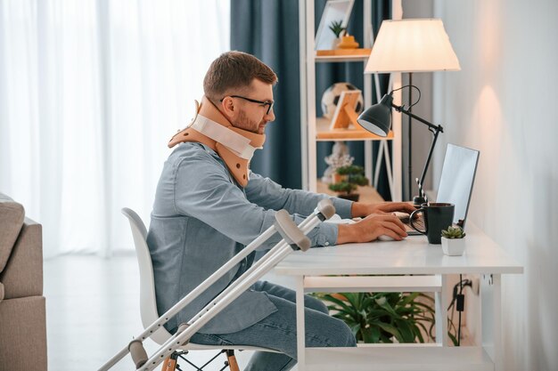 Trabajar desde casa usando una computadora portátil El hombre con muletas está adentro Tiene lesiones