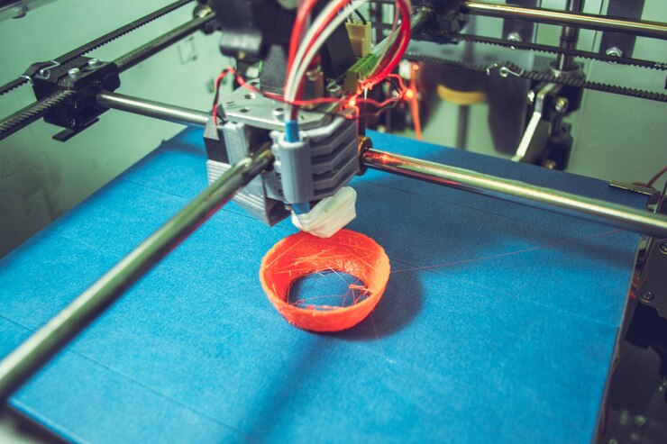 Foto trabajar cerca de la impresora 3d. impresión de la impresora 3d objeto plástico naranja sobre fondo azul. filamento de alambre de plástico, tecnología de impresión moderna. tecnología aditiva progresiva