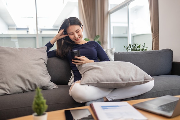 Trabajar desde el concepto de casa una joven empresaria sentada en un acogedor sofá usando su teléfono móvil charlando con los clientes.