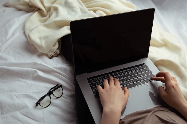 Trabajar en el concepto de casa. Mujer escribiendo en su computadora en la cama.