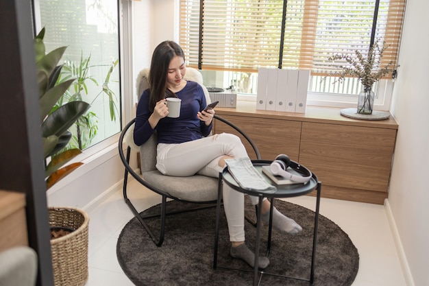 Trabajar desde el concepto de casa una mujer segura de sí misma sentada en una silla moderna sostener una taza de café y otra