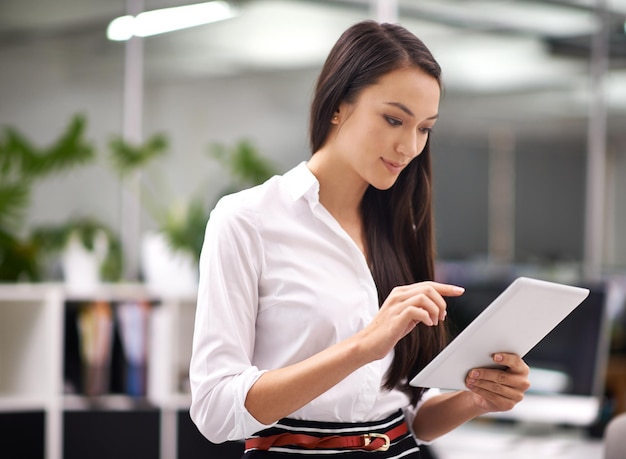 Trabajar es fácil cuando mi oficina está en mi mano Captura recortada de una mujer joven y atractiva que usa una tableta digital en la oficina