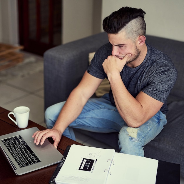 Trabajar horas extra lo acerca a su objetivo Foto de un joven motivado que usa su computadora portátil para trabajar desde casa