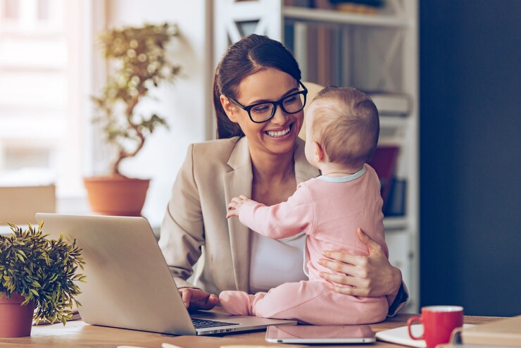 Foto ¡trabajar juntos es muy divertido! alegre joven empresaria hermosa mirando a su bebé con una sonrisa mientras está sentada en su lugar de trabajo