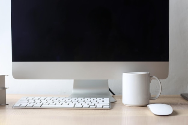 Trabajar con un ordenador de escritorio con pantalla en blanco, un teclado, un ratón y una taza o taza blanca con espacio para copiar