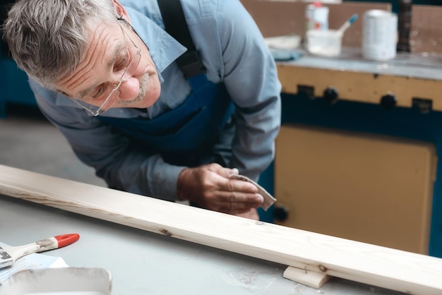 El trabajo del carpintero en el taller de carpintería Un ebanista masculino mayor examina cuidadosamente una tabla de madera