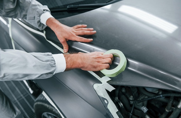 Trabajo detallado Reparador de automóviles caucásico en uniforme tiene trabajo en garaje