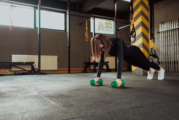 Trabajo duro femenino en el gimnasio con flexiones con mancuernas Mujer fuerte en el gimnasio