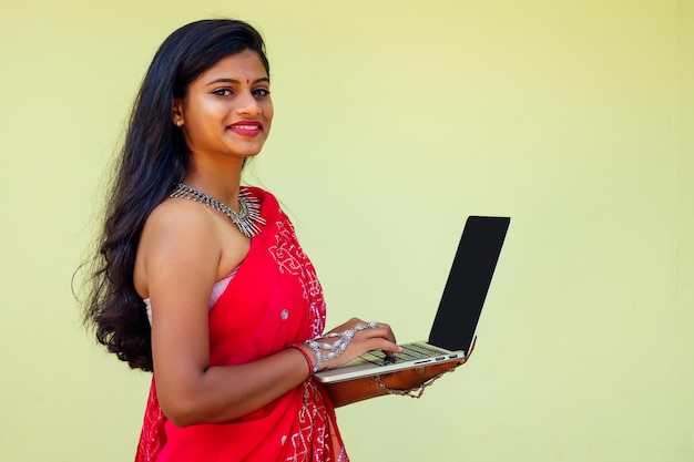 Trabajo de ensueño de concepto de trabajo remoto. mujer de negocios india con sari rojo elegante, peinado rizado, sonrisa blanca con dientes y flor en el cabello trabajando con una computadora portátil mientras se sienta en un café de verano junto al mar