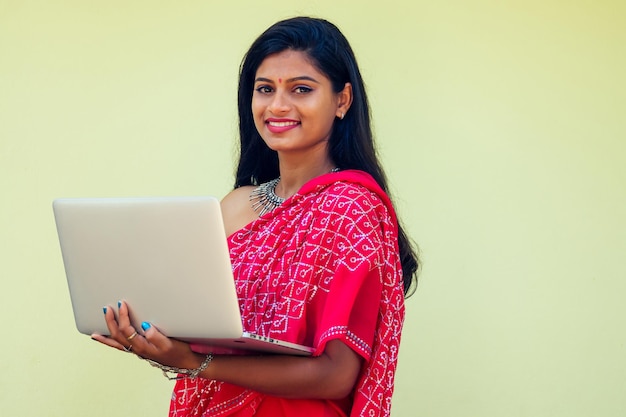 Trabajo de ensueño de concepto de trabajo remoto. mujer de negocios india con sari rojo elegante, peinado rizado, sonrisa blanca con dientes y flor en el cabello trabajando con una computadora portátil mientras se sienta en un café de verano junto al mar