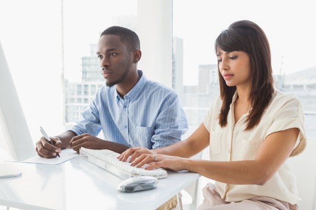 Trabajo en equipo concentrado usando la computadora y tomando notas