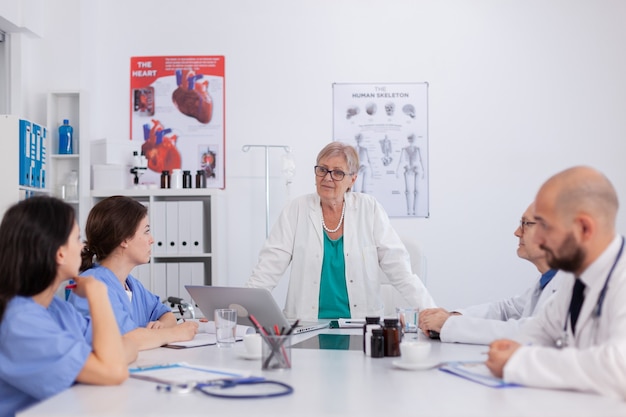 El trabajo en equipo de los médicos en batas blancas que trabajan en la experiencia médica sanitaria en la sala de reuniones de conferencias que presenta el diagnóstico de enfermedad