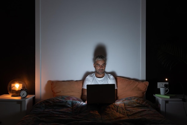 Foto trabajo independiente desde el concepto de hogar hombre hispano trabajando en una computadora portátil a altas horas de la noche sentado en la cama