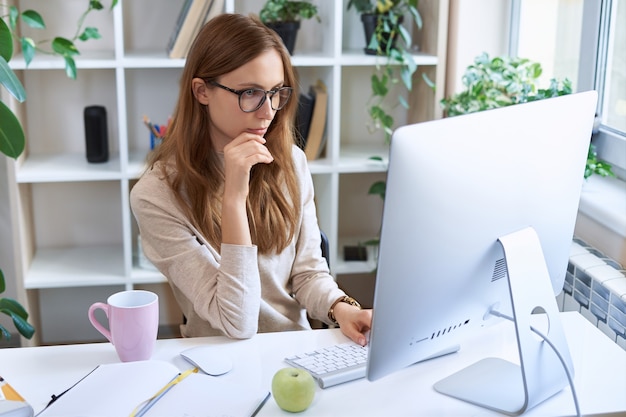 Trabajo en línea joven empresaria concentrada empleada atractiva en gafas sentado en el escritorio