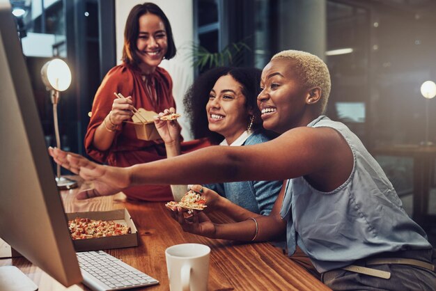 Trabajo nocturno feliz y mujeres con comida para una fecha límite de coworking y horas extra con una propuesta de computadora Riendo divertidos memes y gente de negocios leyendo la comunicación en una PC mientras comen en el turno de tarde