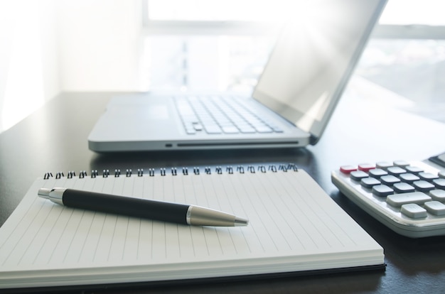 Trabajo de oficina con la pluma, el cuaderno, la calculadora y la computadora portátil en la tabla.