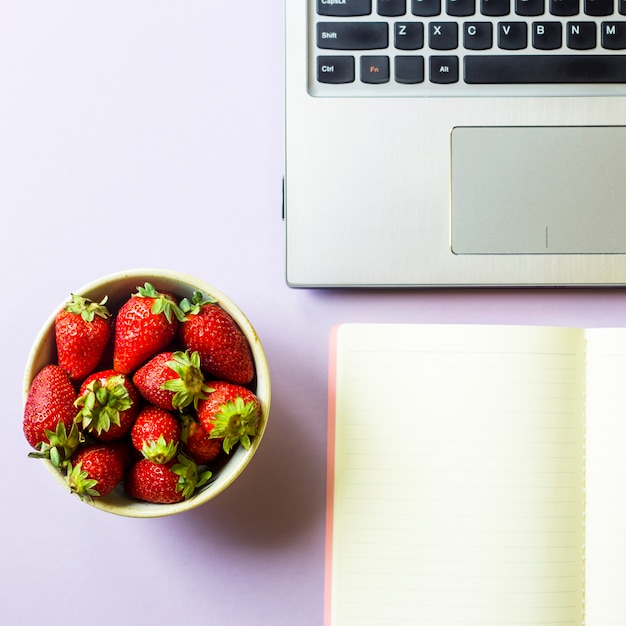 Trabajo de primavera con laptop, notebook y un tazón de fresas.