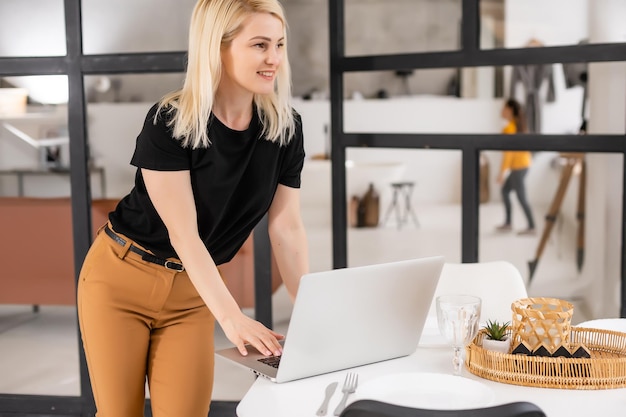 Trabajo remoto en casa, autónomo durante la cuarentena de covid-19. Mujer sonriente sentada y trabajando en una laptop en el acogedor salón interior, espacio libre.