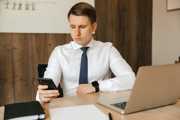 Trabajo remoto en la computadora. Distraído del trabajo, un hombre mira la red social en un teléfono inteligente.