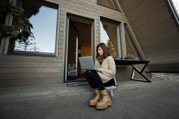 Trabajo remoto y concepto de escape a la naturaleza La mujer trabaja en una computadora portátil contra una pequeña cabaña