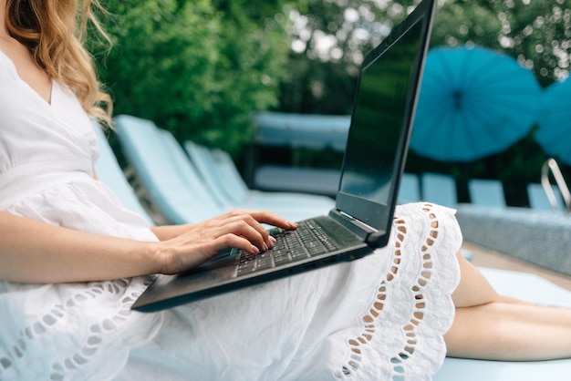 Trabajo remoto de una mujer independiente o empresaria que trabaja en una computadora portátil cerca de la piscina Primer plano de la mano de una dama escribiendo en el teclado Creando un proyecto de vacaciones Vista lateral