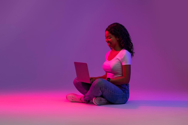 Trabajo remoto mujer negra sonriente usando laptop en luz de neón