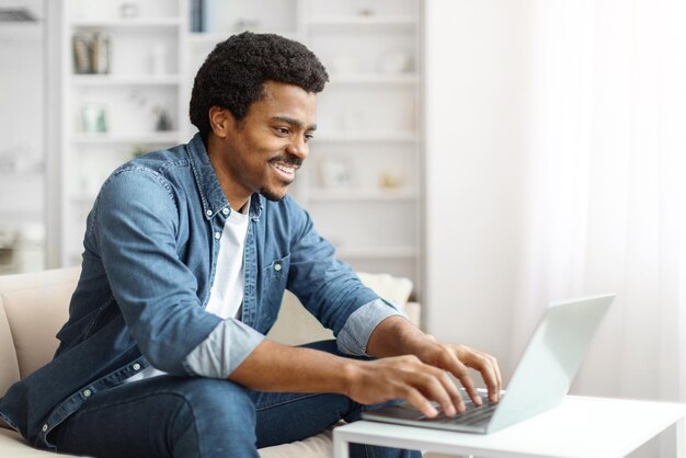 Trabajo remoto sonriente hombre negro freelance trabajando con computadora portátil en casa