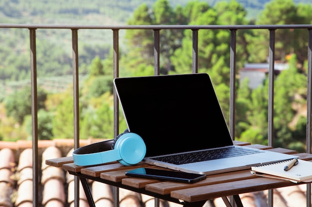 Trabajo desde la terraza de la casa, mesa en la terraza con auriculares portátiles y bloc de notas.