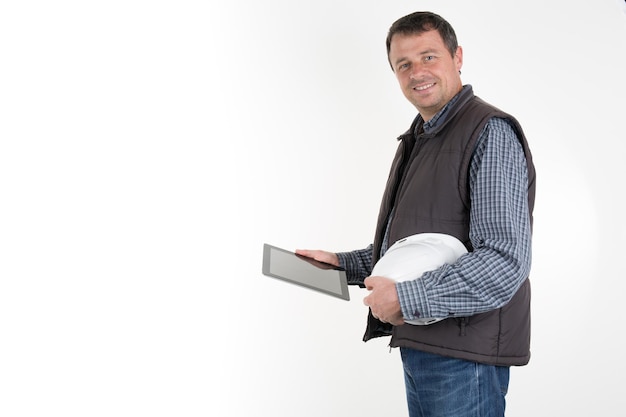Trabalhador alegre no capacete branco e colete marrom segurando tablet digital à prova de choque em ambas as mãos.