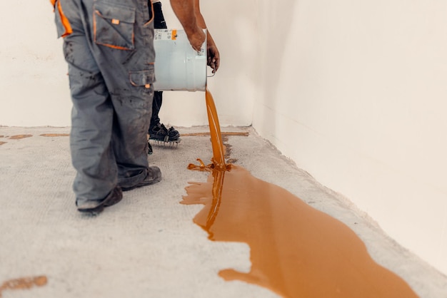 Trabalhador aplicando um balde de resina epóxi amarela no chão