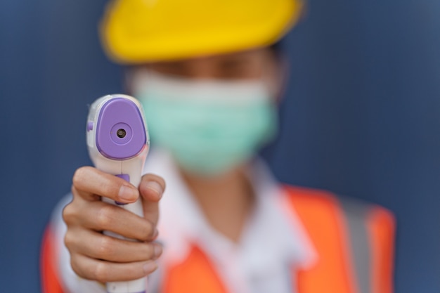 Foto trabalhador asiático com máscara facial usando termômetro infravermelho sem contato