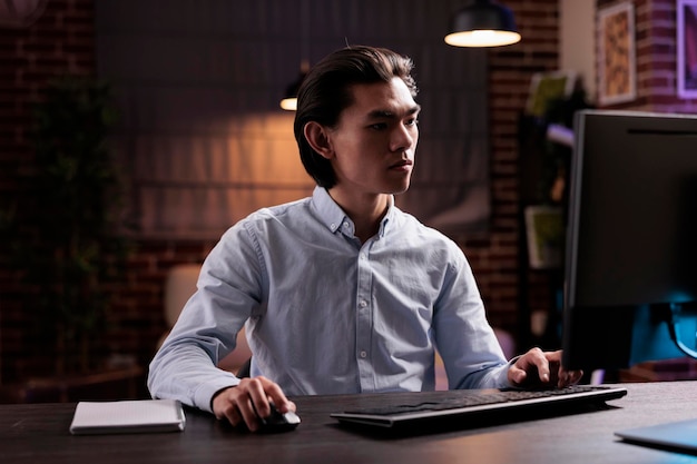 Trabalhador asiático trabalhando em tarefas freelance, criando relatórios de negócios em computador e planejando informações de projetos de pesquisa. Usando o monitor na mesa de casa para planejar a apresentação da gestão da empresa remotamente.