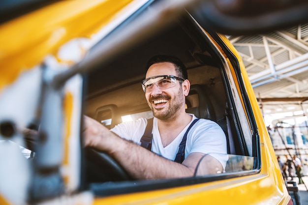 Trabalhador com barba bonito sorridente dirigindo veículo no canteiro de obras.