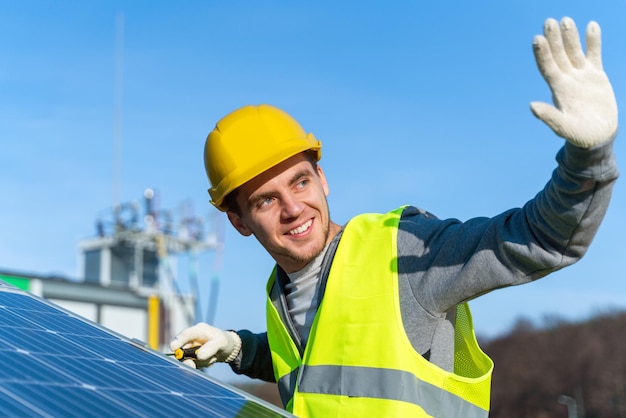 Trabalhador com capacete e equipamento de segurança acenando para alguém enquanto instala e trabalha na manutenção do sistema de painel fotovoltaico instalado