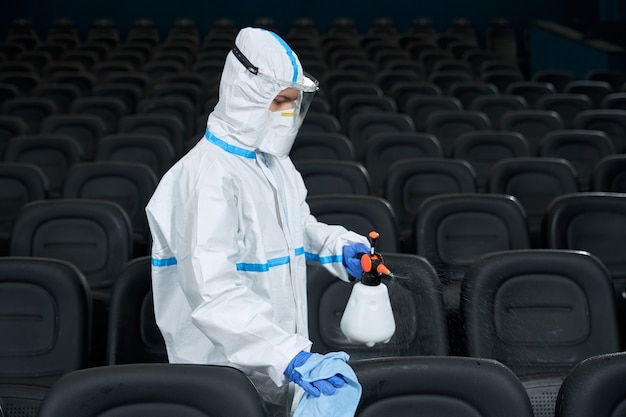 Trabalhador com roupas protetoras limpando a sala do cinema