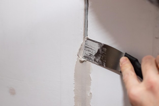 Trabalhador consertando rachaduras no teto espalhando gesso usando espátula rebocando cimento na parede