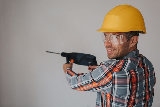 Foto trabalhador construtor com equipamento fazendo um buraco na parede no canteiro de obras