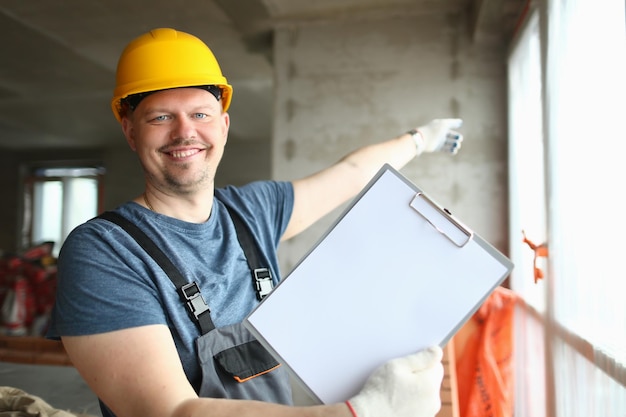 Trabalhador construtor sorridente no capacete segurando uma folha de papel em branco na área de transferência