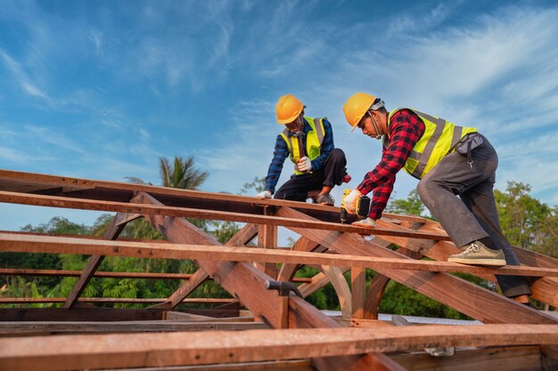 Trabalhador da construção civil asiático instala novo telhado, ferramentas para telhados, furadeira elétrica usada em novos telhados de estrutura de telhado de madeira, conceito de construção de trabalho em equipe.