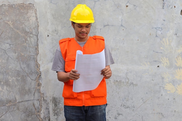 Trabalhador da construção civil com capacete amarelo e colete laranja em um canteiro de obras leu os planos