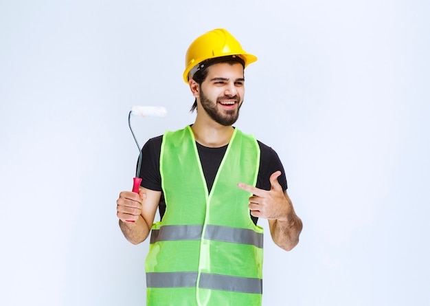 Trabalhador da construção civil com um capacete amarelo segurando um rolo aparador branco.