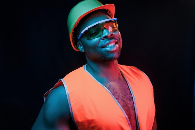 Trabalhador da construção civil de uniforme e capacete de segurança Iluminação neon futurista Jovem afro-americano no estúdio